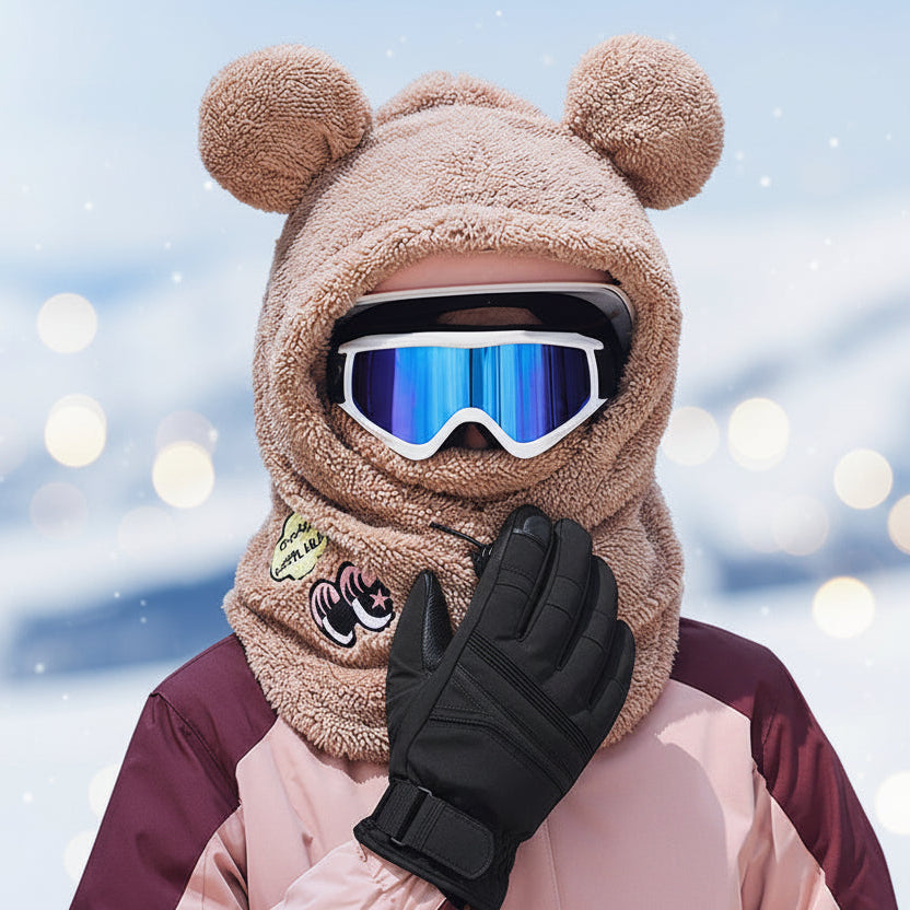 Person wearing a brown bear-themed hood with goggles and gloves in an winter setting